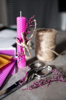 Pink beeswax candle with twine wreath on crafting table.