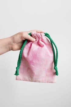 Hand holding pink drawstring bag with green rope against white background.