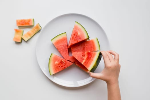 Child hand reaching for watermelon slices on a white plate.