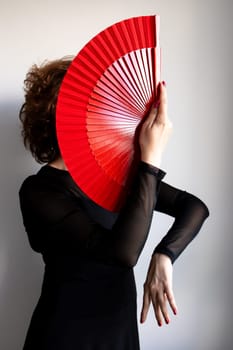 Female dancer with red fan in elegant black attire.