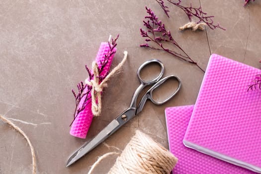 Crafting supplies with pink beeswax candles, scissors, and twine on brown surface.