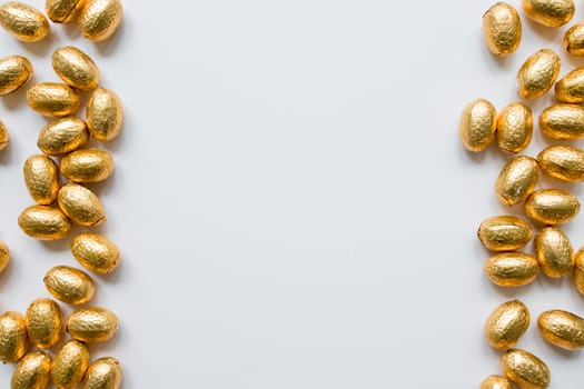 Golden foil wrapped chocolate eggs on white background with creative border.