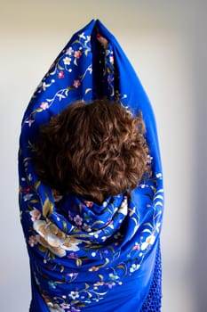 Back view of young caucasian female wrapped in blue floral scarf with curly hair.