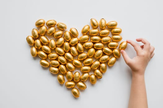 Hand arranging gold foil easter eggs into heart on white background.