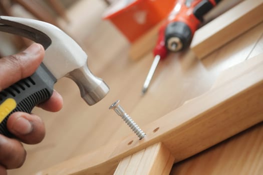 Person uses a hammer to drive a screw into a wooden surface.