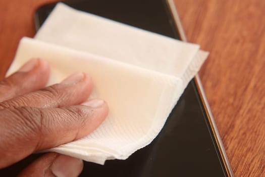 Person wipes a smartphone screen using a clean tissue on a table.