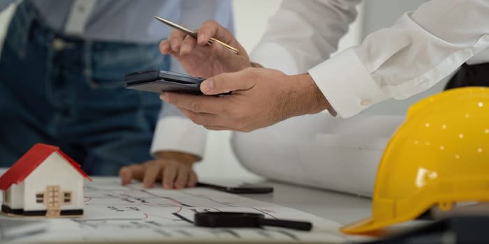 A designer utilizes a calculator while reviewing architectural plans, symbolizing the integration of technology in modern construction processes.