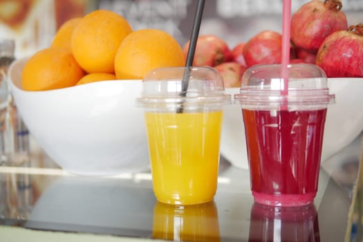 Two colorful fruit juices are served with fresh oranges and pomegranates.