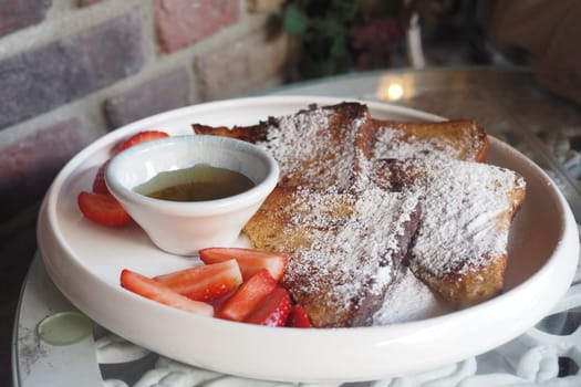 French toast is plated alongside fresh strawberries and syrup.