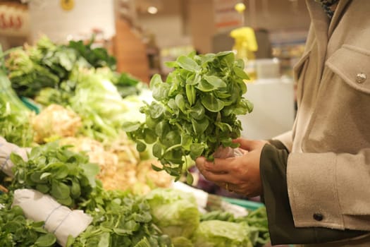 A woman is carefully choosing fresh greens at a market stand.