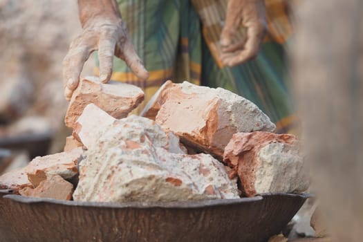 A person skillfully picks up clay bricks from a metal dish while working.