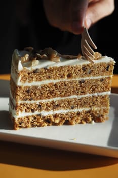 A person carefully adds a fork to a slice of layered dessert.