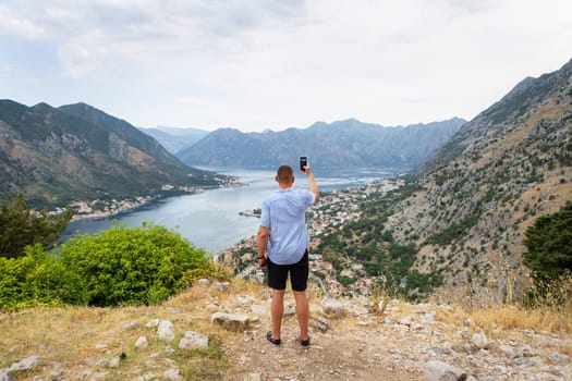 A man takes a photo of a stunning bay view from a mountaintop, capturing the picturesque landscape with his phone.