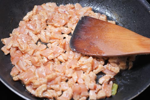 Chopped chicken is sizzling in a skillet, being stirred with a wooden spatula.