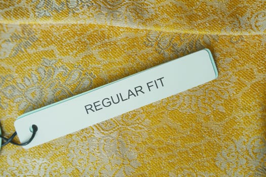A tag labeled regular fit rests on textured yellow fabric showing design.