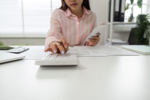 At her home office, a woman actively engages in budgeting, using a calculator while holding a stack of receipts.