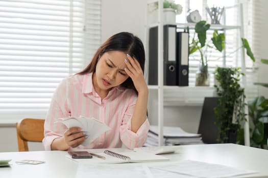 Seated at a table in her home office, a woman looks troubled while reviewing her bills and calculating her financial details, emphasizing the reality of budgeting.