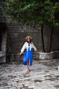 A girl in a blue dress and a straw hat walks through the old town of Europe