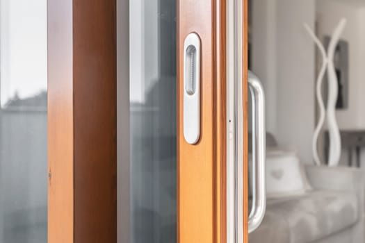 Wooden window open detail. Bottom hung window. Wooden, Metal, PVC door frame closeup view. Stylish chrome handle. Energy efficient and safety profile. Residential garden blurred background.