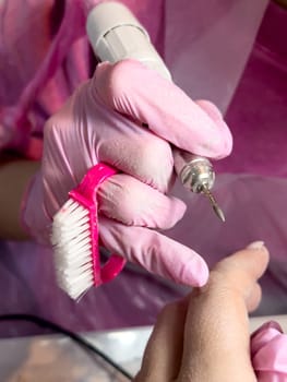 Professional manicure process with pink gloves and nail drill on client hand.