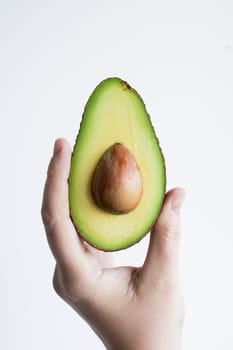 Hand holding fresh half avocado with seed on white background.