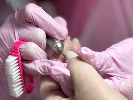 Professional manicure process with electric nail file and pink gloves.