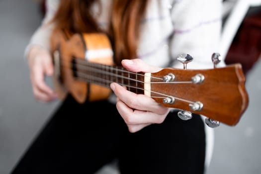 Caucasian female playing ukulele with focus on fingerpicking technique.