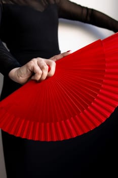 Female hand holding red fan with black dress detail.