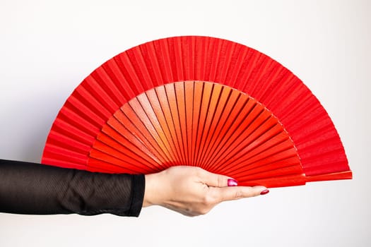 Caucasian female hand holding large red fan against white background.