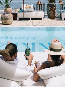 Man and woman with cocktails lie on a double deck chair by the pool. Back view. High quality photo