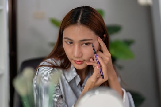 In a moment of concentration, a woman applies eyeliner with precision, enhancing her eyes to achieve a flawless makeup look.