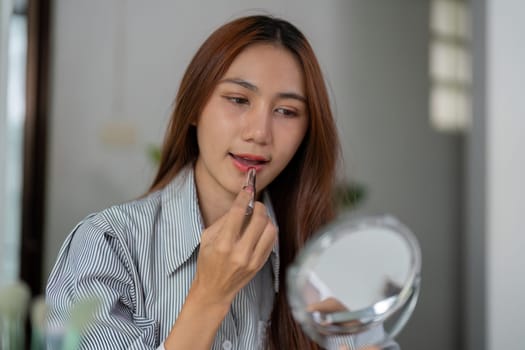 Concentrating on her reflection, a woman enhances her lips with lipstick, showcasing vibrant colors and personal expression during her beauty routine.