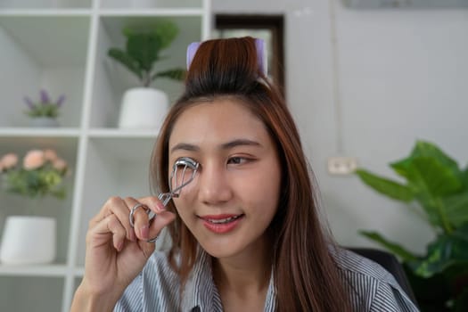 A young woman uses an eyelash curler, looking into the mirror while perfecting her eye makeup for a captivating appearance.