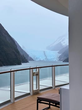 A peaceful cruise ship balcony overlooks a dramatic blue glacier flowing between misty mountains, offering a stunning view of icy wilderness in Patagonia.