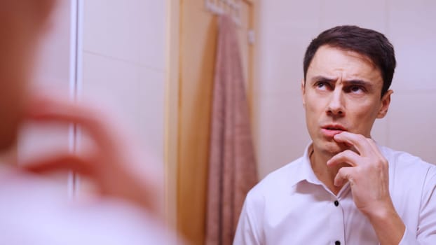 Businessman looking in the mirror with a pensive expression, touching his lips with his fingers