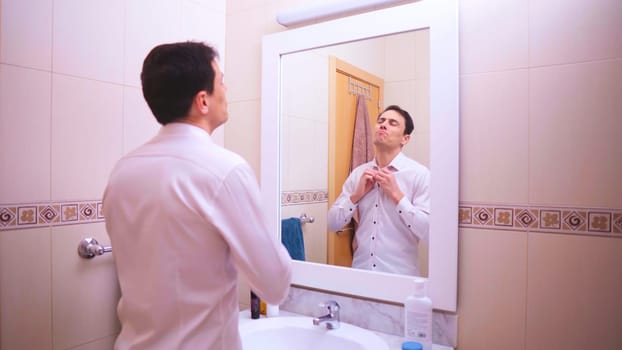Optimistic businessman buttoning his white shirt in the bathroom, getting ready for the workday