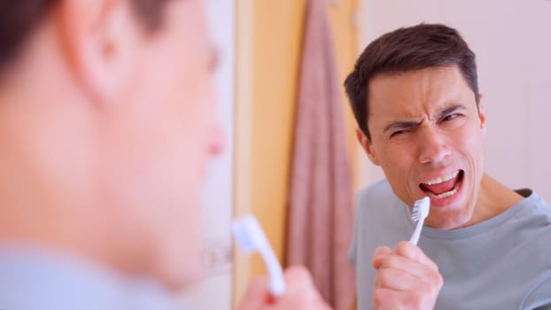 Man using toothbrush as microphone while singing in front of bathroom mirror