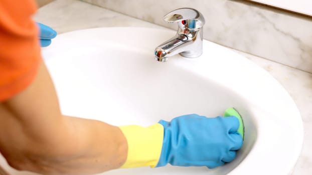 Janitor wearing gloves cleaning white sink with green sponge