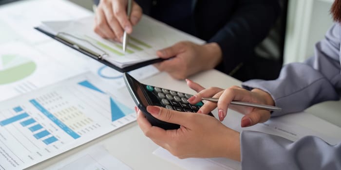 Two professionals analyze data together, one using a calculator to perform calculations, showcasing teamwork in financial analysis and reporting.