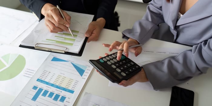 Two colleagues collaborate on data reporting, calculating figures and analyzing charts to drive business decisions in a professional setting.