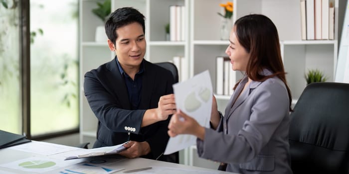 Two professionals exchange reports during a meeting, reinforcing their collaboration in understanding and analyzing financial data.