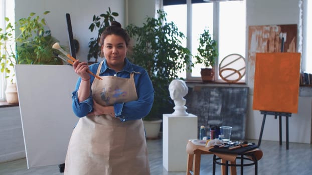 A woman painter posing with brushes in hand and looking in the camera. Mid shot