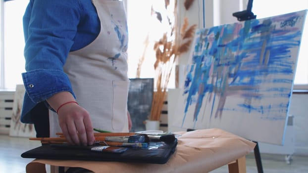 A woman paint artist taking a brush from the table. Mid shot