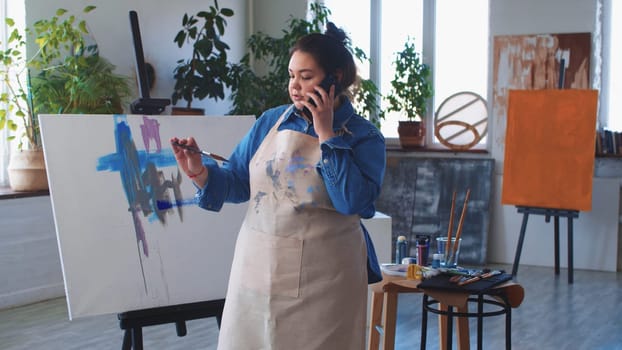 A woman paint artist talking in her phone while drawing a painting. Mid shot