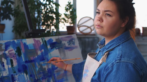 A woman artist drawing a painting and looking to the side. Mid shot