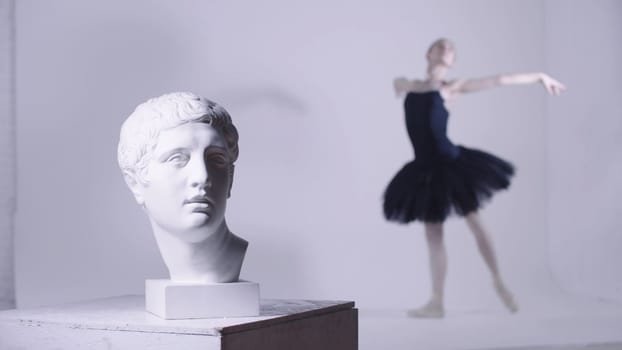 Young woman ballerina in black dress training - a head of greek sculpture on the foreground. Mid shot