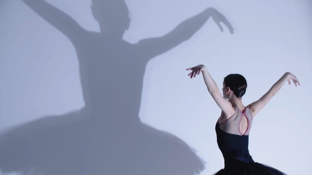 Young woman ballerina in black dress dancing - a big shadow on the wall. Mid shot