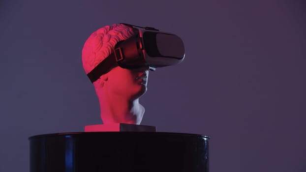 A greek head sculpture in VR glasses on the stand - red lighting. Mid shot