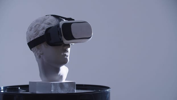 A greek head sculpture in VR glasses on the stand. Mid shot
