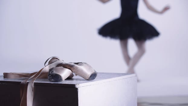 Young woman ballerina in black dress dancing in white studio - pointe shoes on the foreground. Mid shot